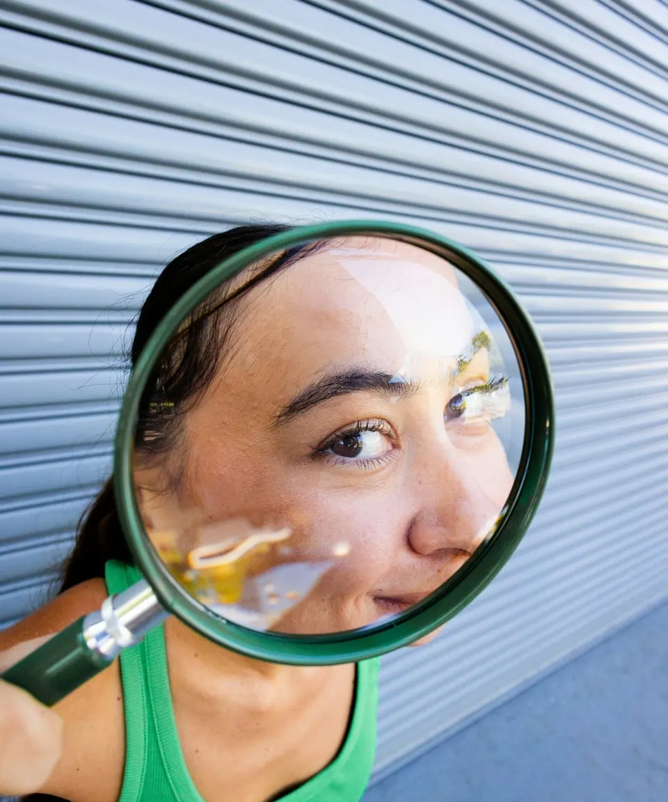 Young woman looking curiously through a magnifying glass